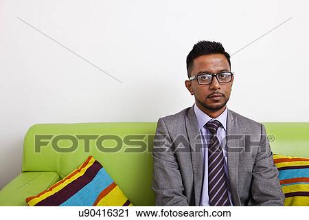 Stock Image - Businessman sitting on sofa looking at camera. Fotosearch