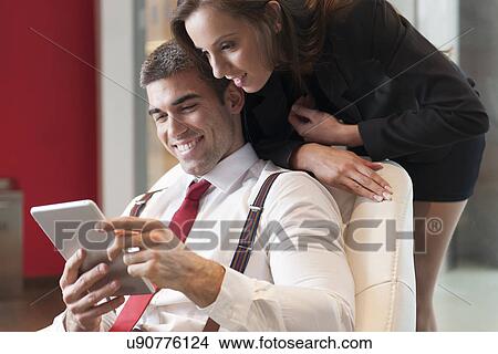 Picture - Businesswoman looking over male colleagues shoulder pointing at digital tablet. Fotosearch