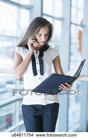 Picture - Businesswoman on mobile phone reading from folder. Fotosearch