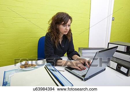 Picture - Caucasian young woman working on her laptop computer at her desk. Fotosearch