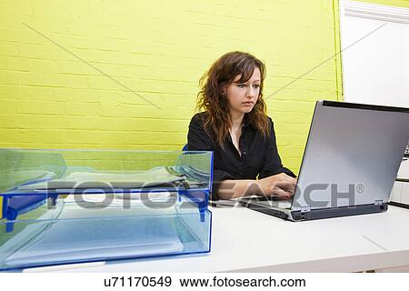 Caucasian young woman working on her laptop computer at her desk View Large Photo Image Stock Photo - Caucasian young woman working on her laptop computer at her desk. Fotosearch
