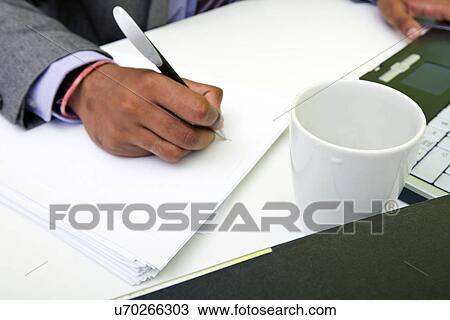 Stock Image - Close up of Indian mans hands writing on paper.. Fotosearch