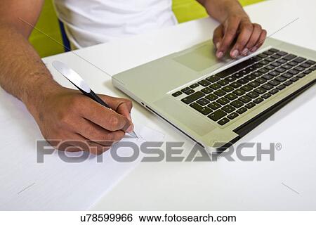 Close up of Indian mans hands writing on paper next to laptop View Large Photo Image Stock Photograph - Close up of Indian mans hands writing on paper next to laptop. Fotosearch