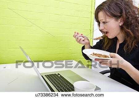 Picture - Close up of woman eating at her desk. Fotosearch