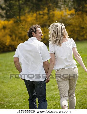 Couple holding hands with back to camera running through park View Large Photo Image Stock Photo - Couple holding hands with back to camera running through park. Fotosearch