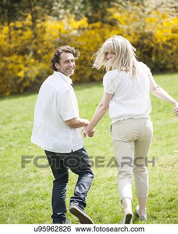 Couple holding hands with back to camera running through park View Large Photo Image Stock Photograph - Couple holding hands with back to camera running through park. Fotosearch