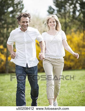 Stock Image - Couple running through park holding hands. Fotosearch