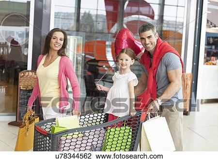 Stock Image - Father and mother push young daughter in shopping trolley through mall. Fotosearch