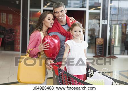 Father and mother push young daughter in shopping trolley through mall View Large Photo Image Stock Photo - Father and mother push young daughter in shopping trolley through mall. Fotosearch