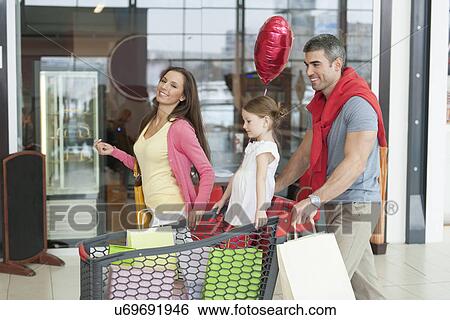 Father and mother push young daughter in shopping trolley through mall View Large Photo Image Stock Photograph - Father and mother push young daughter in shopping trolley through mall. Fotosearch
