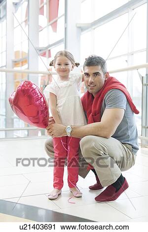Father kneels with younger daughter holding balloon View Large Photo Image Stock Image - Father kneels with younger daughter holding balloon. Fotosearch