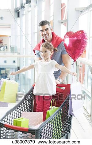Stock Photo - Father pushing young daughter in shopping trolley with shopping bags. Fotosearch