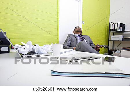 Indian businessman asleep at his desk clutching ukulele View Large Photo Image Stock Image - Indian businessman asleep at his desk clutching ukulele. Fotosearch