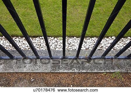 Stock Photograph - Iron fence, grass and pebbles. Fotosearch