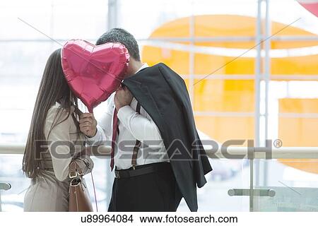 Man and woman kiss behind heart shaped balloon View Large Photo Image Picture - Man and woman kiss behind heart shaped balloon. Fotosearch