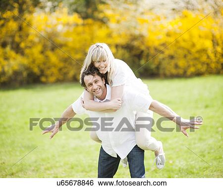 Stock Photograph - Man piggybacking woman in park. Fotosearch