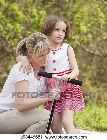 Stock Image - Mother and daughter hug in park with scooter. Fotosearch