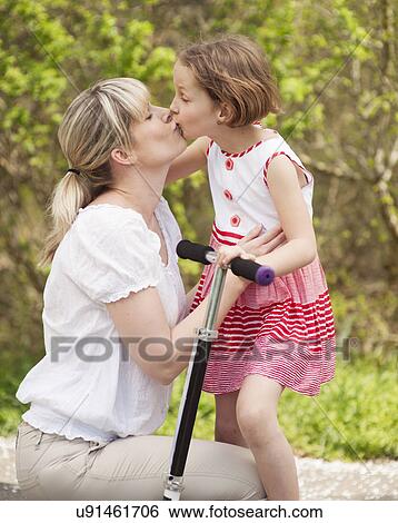 Stock Photograph - Mother and daughter kissing in park with scooter. Fotosearch