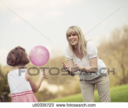 Stock Image - Mother throwing ball to daughter in park. Fotosearch