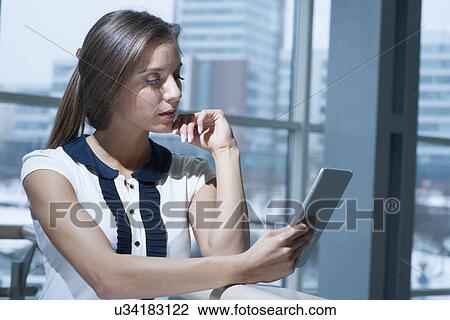 Stock Image - Pensive businesswoman reading from digital tablet. Fotosearch