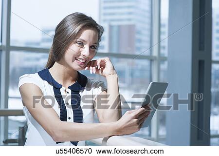 Stock Image - Pensive businesswoman smiling at camera holding digital tablet. Fotosearch