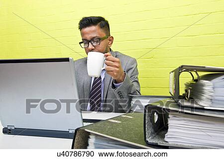 Portrait of Indian Businessman holding mug and working on his laptop computer at his desk View Large Photo Image Stock Image - Portrait of Indian Businessman holding mug and working on his laptop computer at his desk. Fotosearch