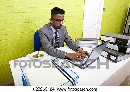 Picture - Portrait of Indian Businessman working on his laptop computer at his desk. Fotosearch