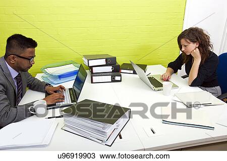 Side view of colleagues working at their desks opposite each other View Large Photo Image Stock Image - Side view of colleagues working at their desks opposite each other. Fotosearch