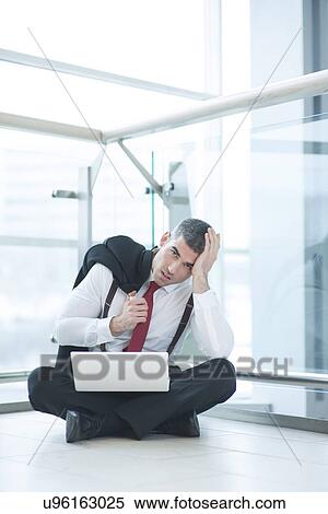 Stock Photography - Stressed out businessman seated on floor working at laptop. Fotosearch