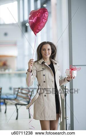 Stock Photo - Woman runs to camera holding heart shaped balloon and gift. Fotosearch