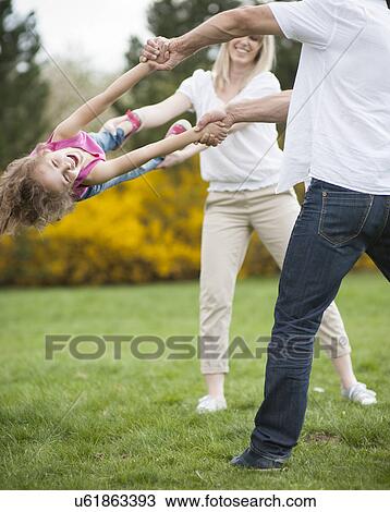 Stock Image - Young couple swinging daughter between them. Fotosearch