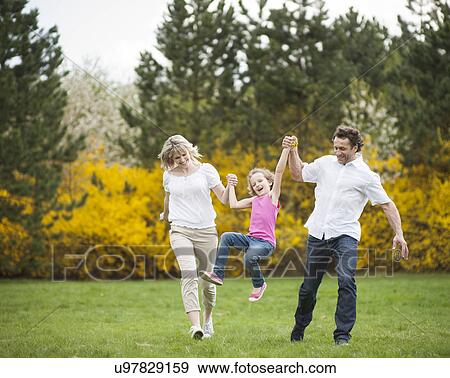 Stock Photo - Young couple swinging daughter between them . Fotosearch