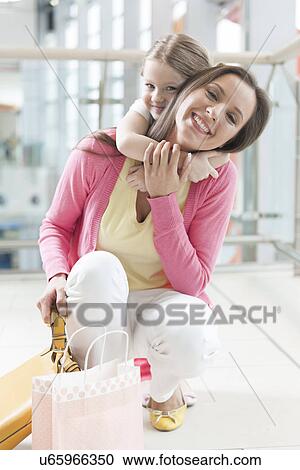 Stock Image - Young daughter hugs mother in shopping mall. Fotosearch