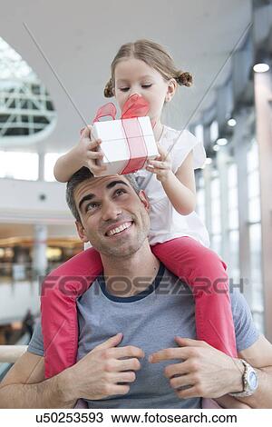 Young daughter sits on fathers shoulders and gives him a present View Large Photo Image Stock Image - Young daughter sits on fathers shoulders and gives him a present. Fotosearch