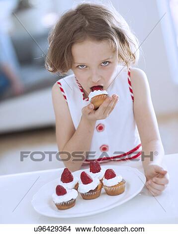Picture - Young girl eating cup cake. Fotosearch
