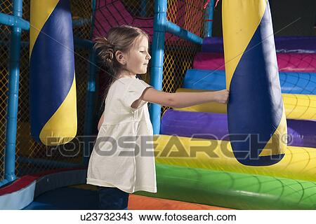 Stock Image - Young girl hitting foam object in play gym. Fotosearch