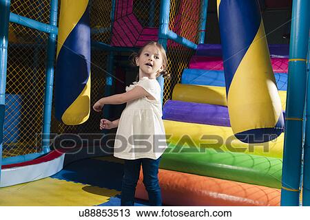 Stock Image - Young girl hitting foam object in play gym. Fotosearch