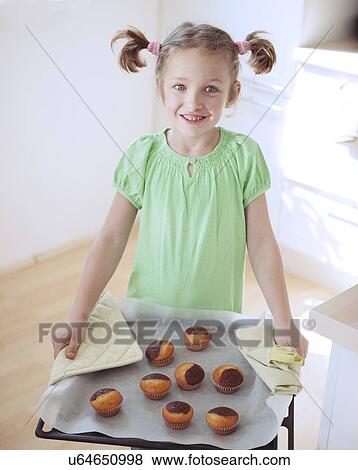 Stock Photo - Young girl holding baking tray in kitchen. Fotosearch