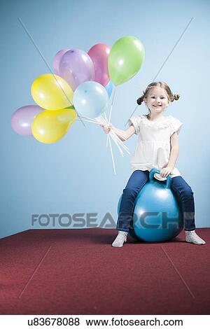 Stock Photo - Young girl holding balloons on a hoppity horse. Fotosearch