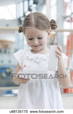 Stock Image - Young girl opens white box and looks into it. Fotosearch