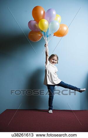 Stock Image - Young girl pretending to be lifted up by bunch of balloons. Fotosearch