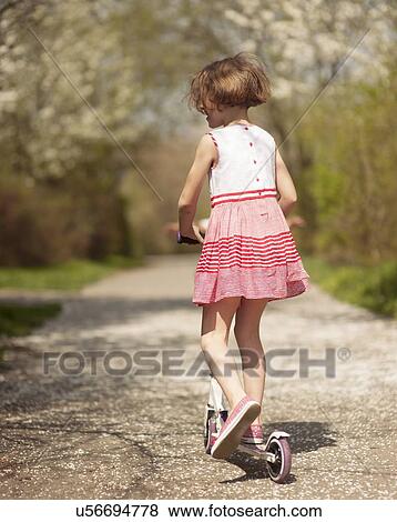 Stock Photo - Young girl riding scooter away from camera on path through park. Fotosearch