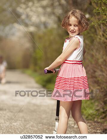 Young girl riding scooter in park away from camera to mother View Large Photo Image Stock Image - Young girl riding scooter in park away from camera to mother. Fotosearch