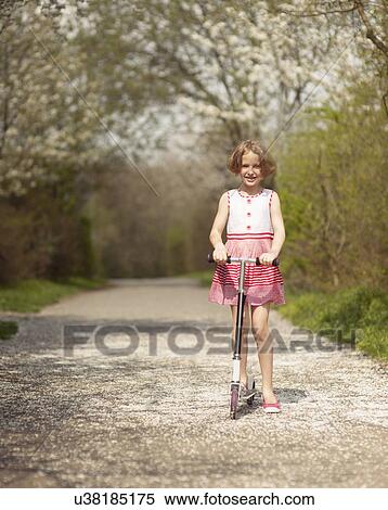 Young girl riding scooter on path through park View Large Photo Image Stock Photography - Young girl riding scooter on path through park. Fotosearch