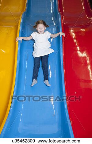 Stock Photo - Young girl slides down colorful slide. Fotosearch