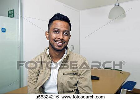 Stock Photograph - Young Indian man smiling at camera in his office . Fotosearch