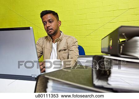 Young Indian man working at his computer surrounded by folders View Large Photo Image Stock Image - Young Indian man working at his computer surrounded by folders. Fotosearch