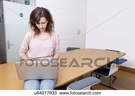 Young woman sitting on table working on laptop View Large Photo Image Stock Image - Young woman sitting on table working on laptop. Fotosearch