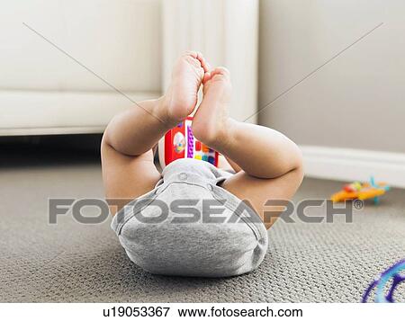 Stock Photo - Baby boy (2-5 months) lying on floor playing. Fotosearch