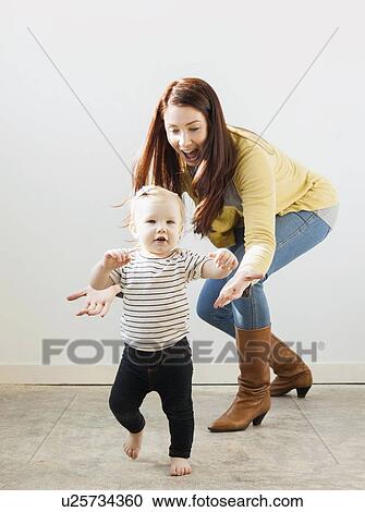 Stock Image - Baby girl (12-17 months) walking while mother assisting her. Fotosearch